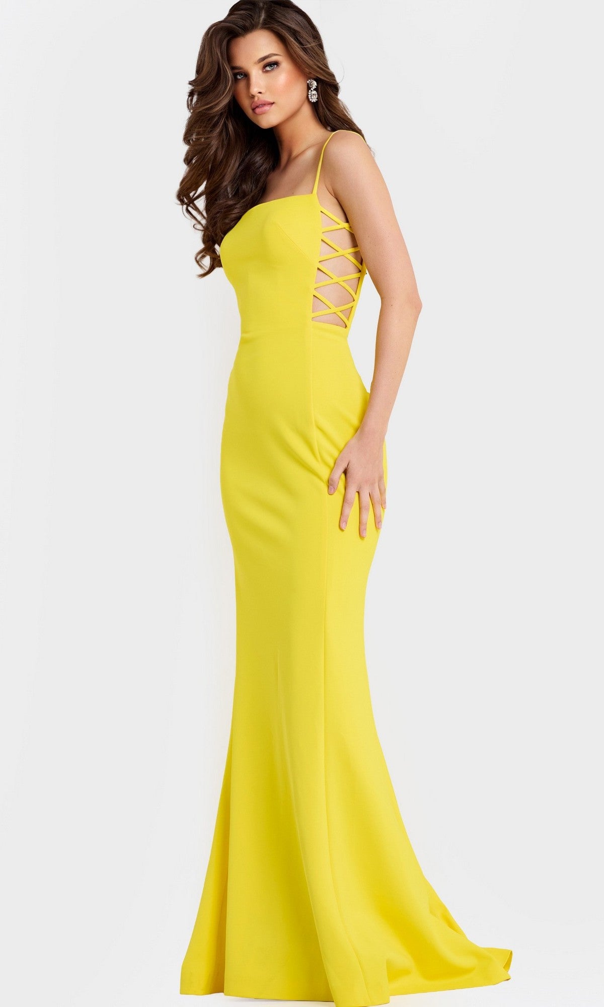 A woman models the Jovani 43404 long prom dress—fitted and floor-length in yellow, with thin straps and criss-cross lace-up sides—against a plain white background.
